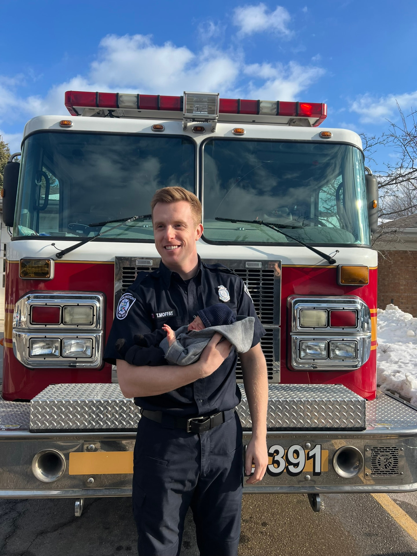 Tom Moffat holding his newborn in front of a fire truck